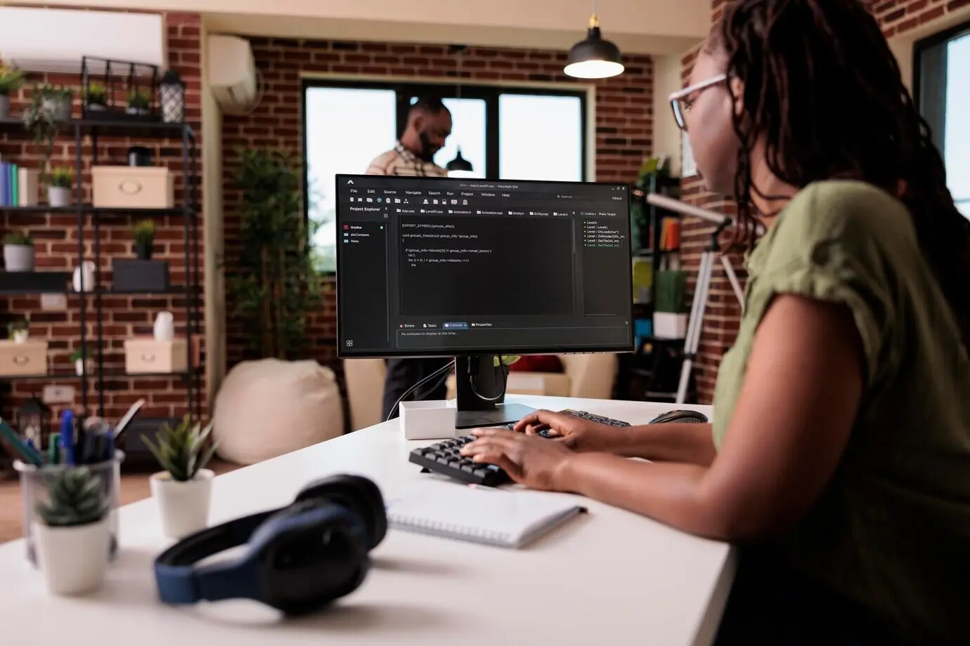 Афроамериканская программистка, работающая удалённо из дома над фриланс-проектом, пишет исходный код и ищет ошибки во время отладки, пока её парень отдыхает.