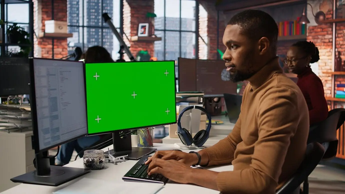 Программист пишет код в офисе ИИ-стартапа, используя ПК с изолированным экраном.